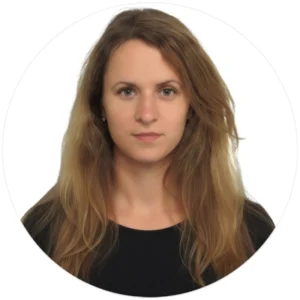 A person with long, wavy, light brown hair wearing a black top, presented in a circular frame.